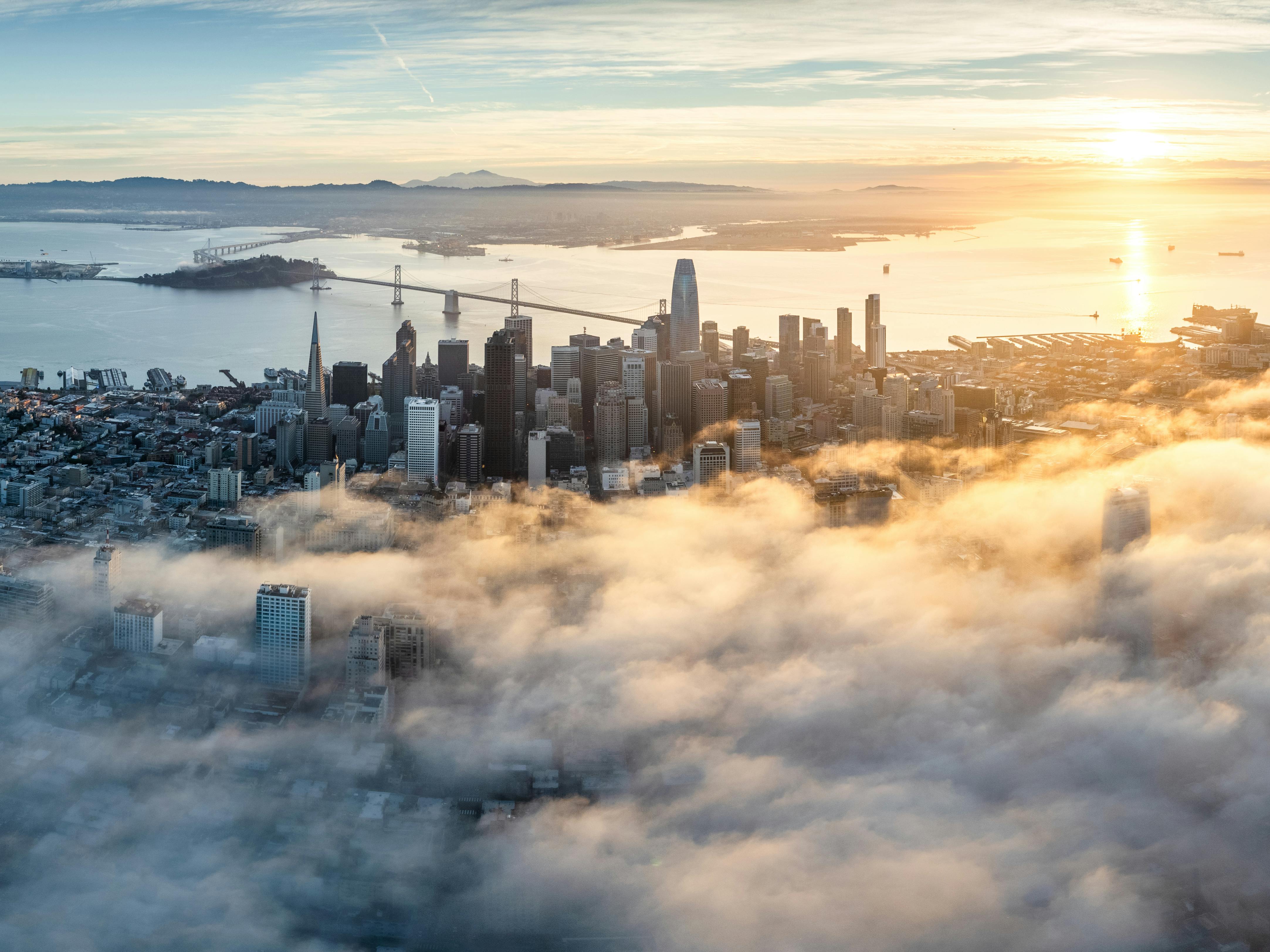 San Francisco skyline at dusk with fog rolling in over the financial district and the Bay Bridge.